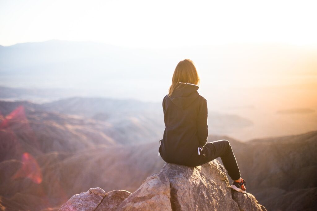 Präsenz als Frau entfalten - eine Frau sitz nachdenklich auf einem Felsen und schaut in den Sonnenaufgang